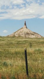 Low angle view of chimney rock in front of grassy field against sky on sunny day