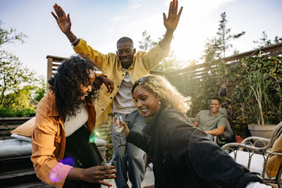 Cheerful multiracial male and female friends dancing together at dinner party in back yard