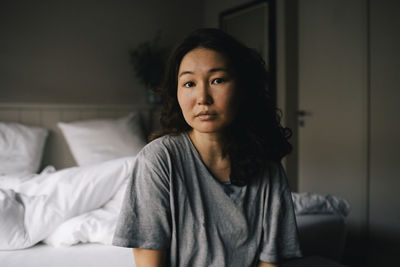 Portrait of sad woman with mental health illness sitting in bedroom at home