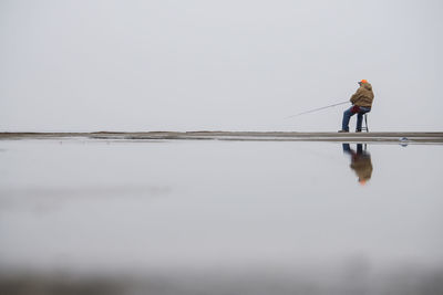 Full length rear view of man sitting on chair at pier