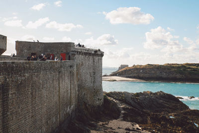 Retaining wall by sea against cloudy sky