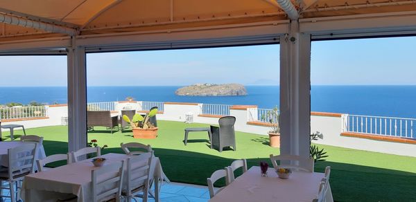 Chairs and table by sea against clear sky