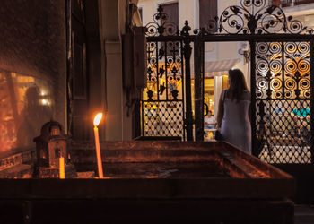 Lit candle on altar in church with woman standing outside gate