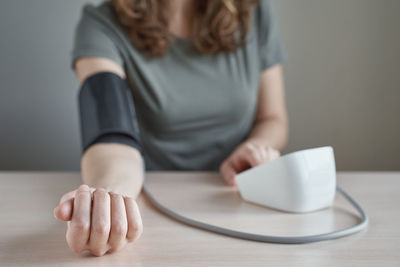 Midsection of woman measuring blood pressure with gauge on table