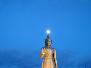 Low angle view of statue against illuminated blue sky