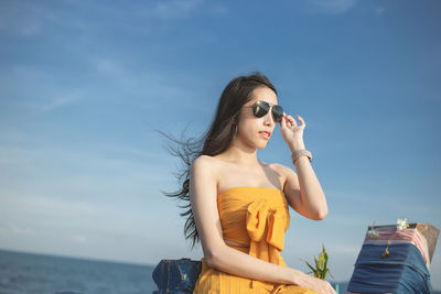 Young woman wearing sunglasses standing against sky