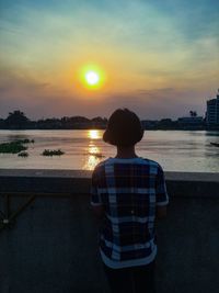 Rear view of man standing by sea against sky during sunset