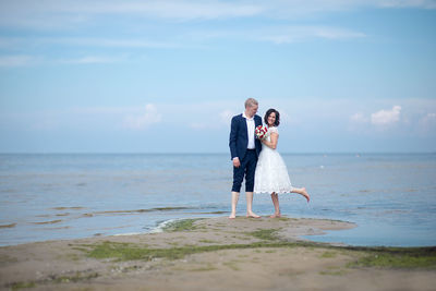 Full length of bride and bridegroom standing at beach