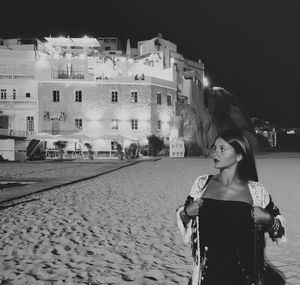 Woman standing on sidewalk in city at night