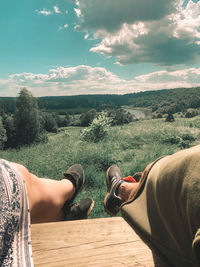 Low section of man relaxing on landscape against sky