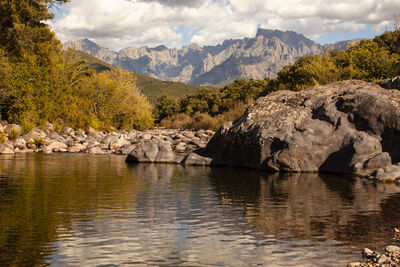 Scenic view of river and rocky mountains against sky