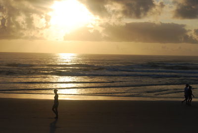 People walking on sand against sea during sunset