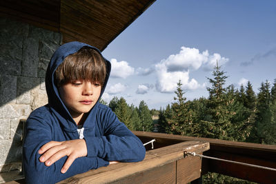 Cute boy wearing hooded shirt while leaning on railing