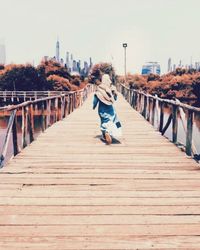 Rear view of woman on footbridge against sky