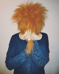 Person covering face with stuffed toy while standing against wall