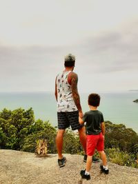 Rear view of man standing with son against sea