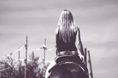 Rear view of woman riding horse against sky