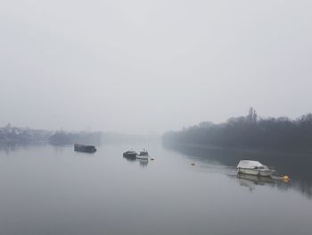 Boats moored in lake against sky during foggy weather