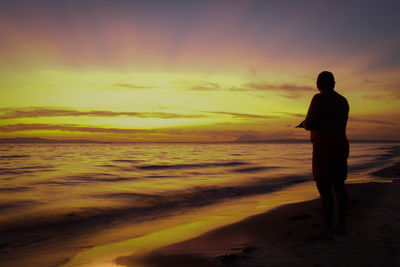 Silhouette man standing on beach against sky during sunset