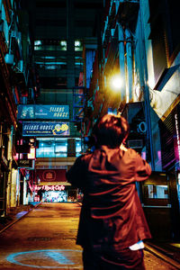 Rear view of man standing on illuminated street at night