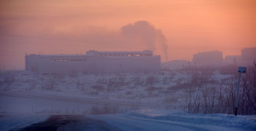 Snow covered city against sky during sunset