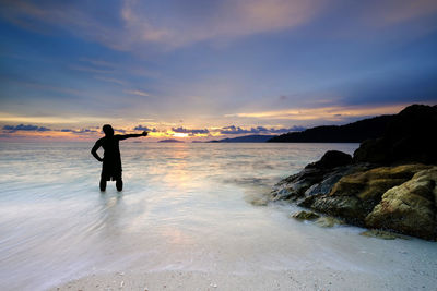 Man standing on beach against sky during sunset