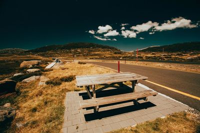 Empty picnic table and bench on roadside against sky