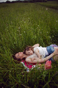 Mother and daughter lie on a green field in summer and relax in the sun