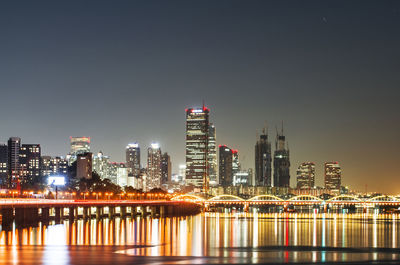 Illuminated buildings by river against sky at night