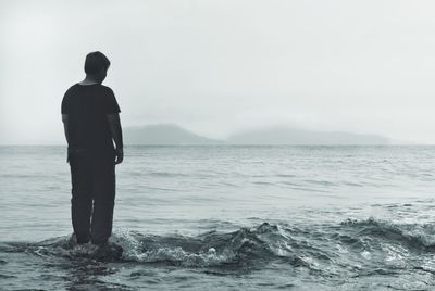 Rear view of man standing in sea against sky