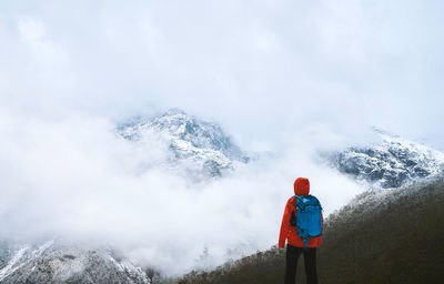 Rear view of man standing on mountain during foggy weather