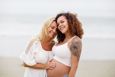 Mom posing with pregnant daughter on beach