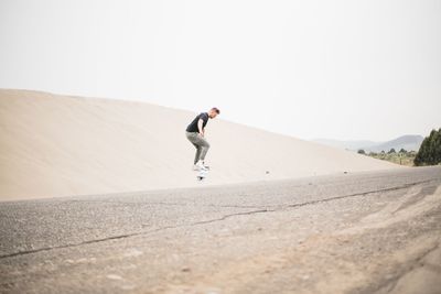 Side view of young man skateboarding at desert