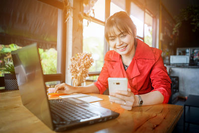 Young woman using phone by laptop while sitting at home