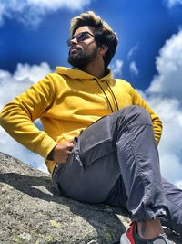 Young man looking away while sitting against sky