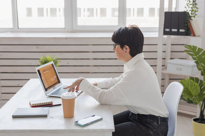 Side view of woman using laptop while sitting on table