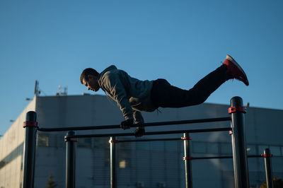 Low angle view of young man jumping against clear sky