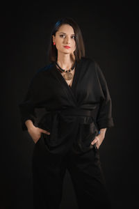 Portrait of young woman standing against black background