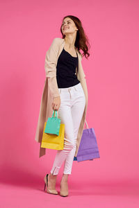 Woman holding shopping bags while standing against pink background