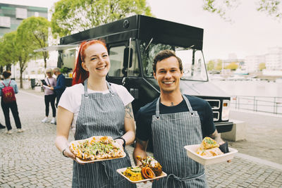 Smiling owner with assistant holding indian food plate in city