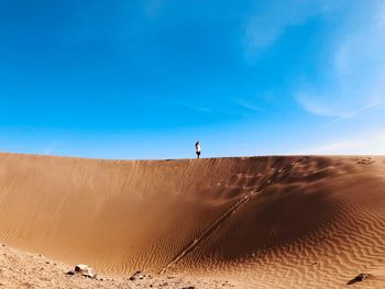 Man on sand dune in desert against blue sky