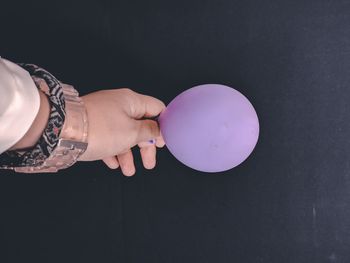 Close-up of hand holding balloons against black background