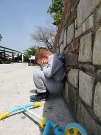 Full length of boy crying while crouching by retailing wall