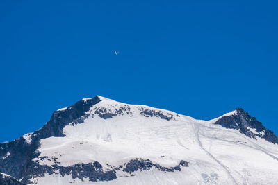 Low angle view of snowcapped mountains against clear blue sky