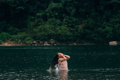 Woman standing in lake against trees