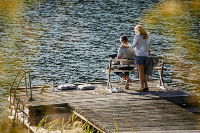 Rear view of people sitting on pier over lake