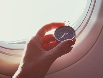 Close-up of hand holding navigational compass by airplane window