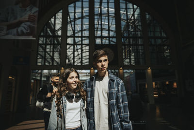 Brother and sister looking away while standing at station during sunny day