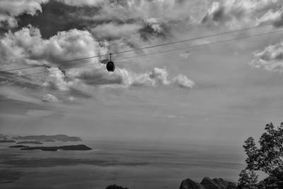 Low angle view of ski lift over sea against cloudy sky