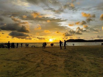 Silhouette people on beach against sky during sunset